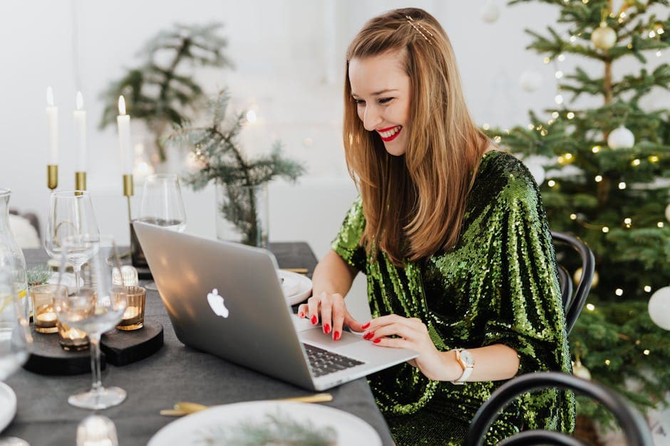 Woman in a green dress smiling while working on a laptop during a Christmas celebration.