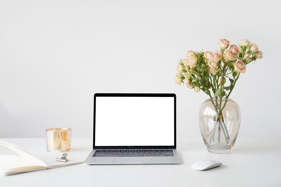 Elegant minimalist workspace featuring a laptop with a blank screen, flowers in a vase, and soft ambient lighting.
